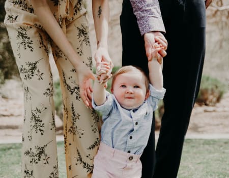 A baby holding hands with two adults.