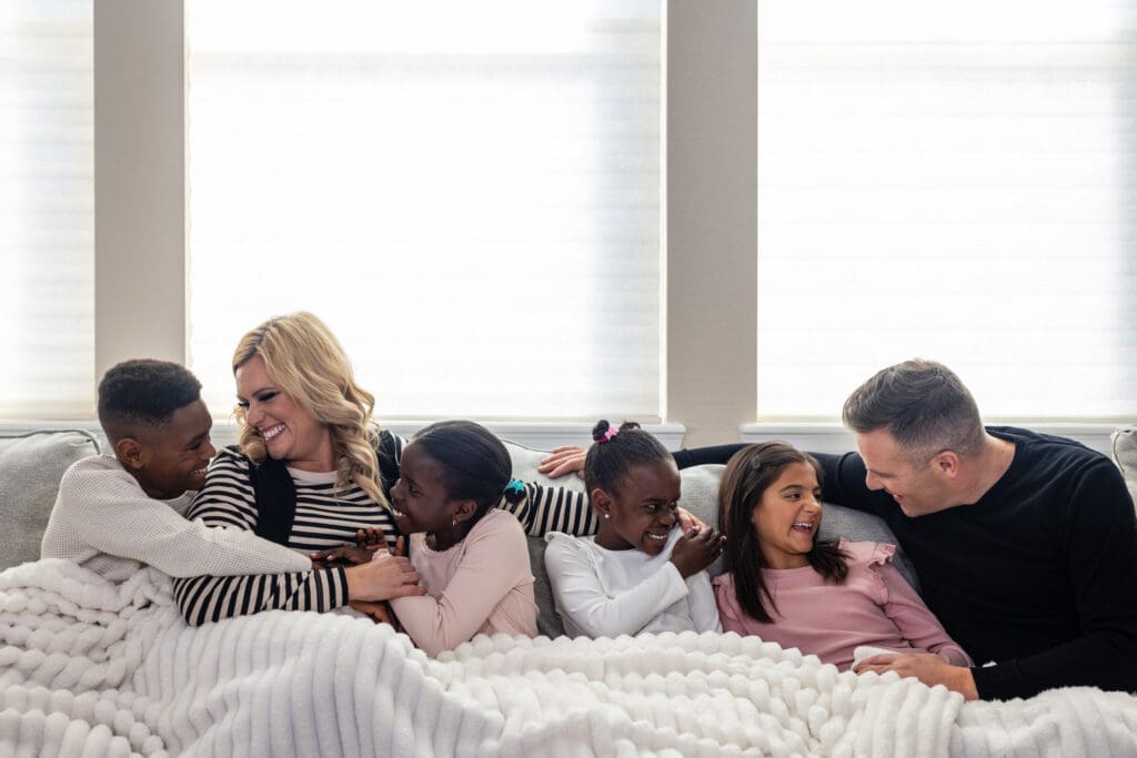 family of 6 snuggled on a couch underneath a blanket